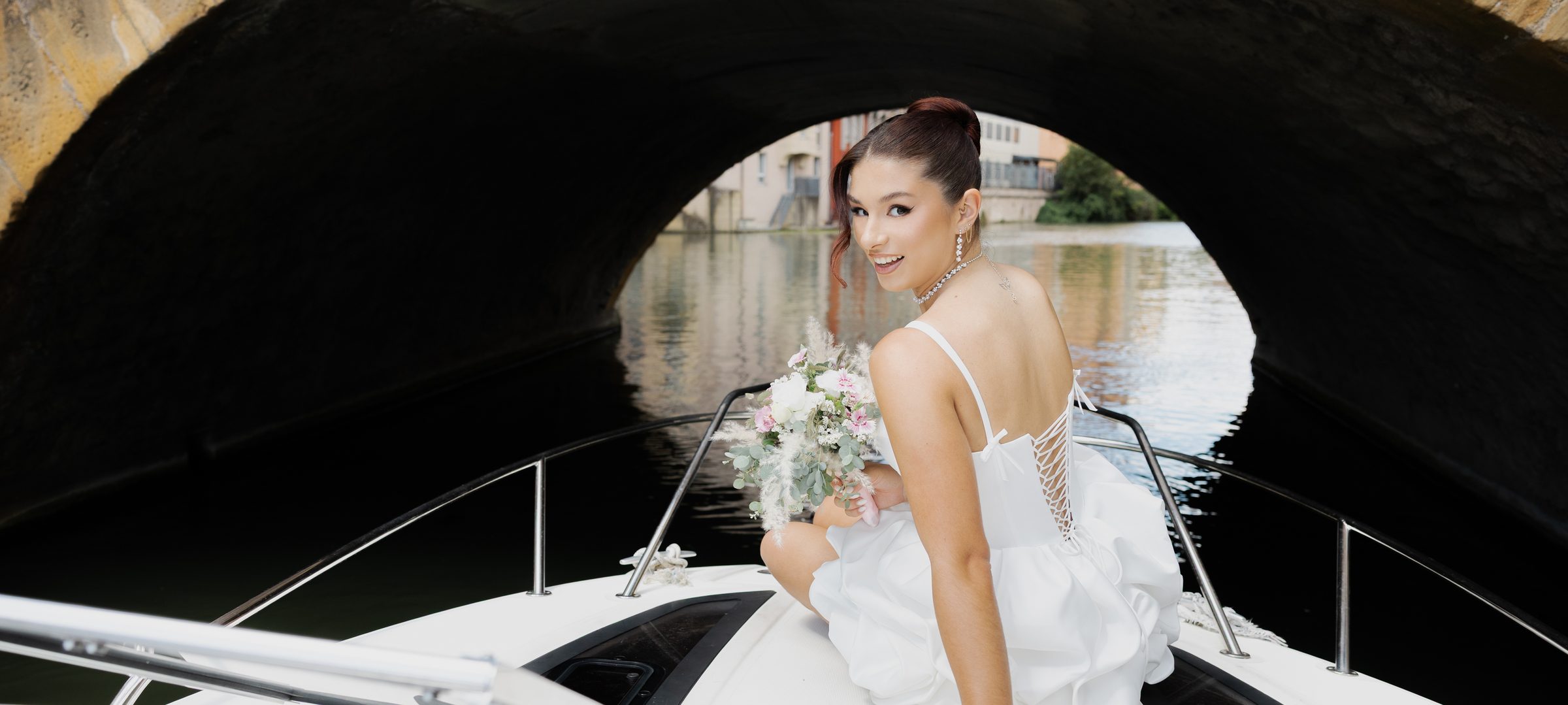 Mariée en robe courte sur un bateau, sous un pont