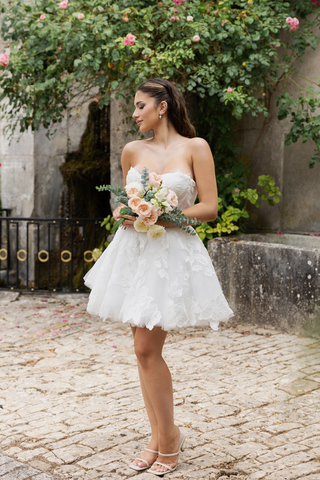 Robe courte à fleurs en relief, devant un mur de rosiers, bouquet
