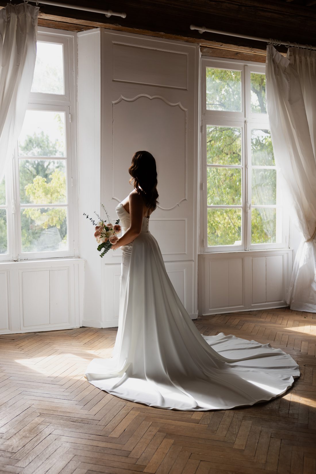 Robe satin à longue traîne, de dos entre deux fenêtres